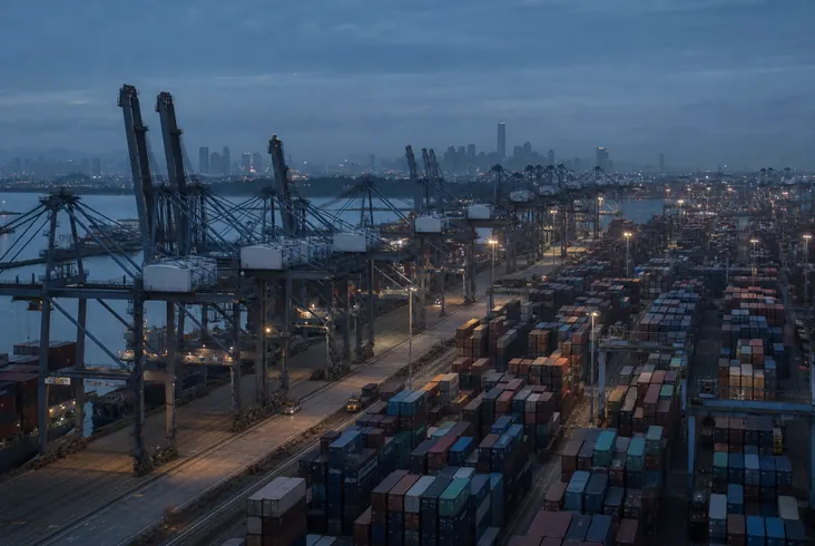 Terminal de contêineres ao entardecer, com guindastes e pilhas de contêineres.
